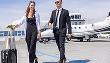 Geschäftspaar steigt am Flughafen Hof-Plauen aus einem Privatjet, im Hintergrund der Tower