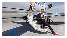 Geschäftsperson sitzt auf der Einstiegstreppe eines Privatjets und checkt E-Mails am Smartphone